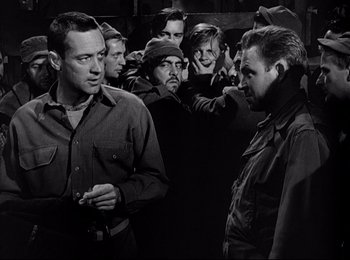 Movie still from “Stalag 17” (1953), directed by Billy Wilder – A black and white photo of a group of men; Medium shot, Over the shoulder angle