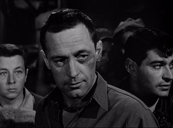 Movie still from “Stalag 17” (1953), directed by Billy Wilder – Black and white photograph of a man in front of a group of men; Close Up shot, Over the shoulder angle