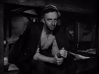 Movie still from “Stalag 17” (1953), directed by Billy Wilder – A black and white photo of a man sitting on the floor; Medium shot, Low angle