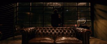 Movie still from “Gunpowder Milkshake” (2021), directed by Navot Papushado – A man standing in a room next to a leather couch; Wide shot, Over the shoulder angle