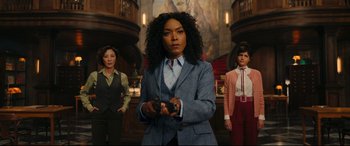 A woman in a suit holding a game controller in front of two other women