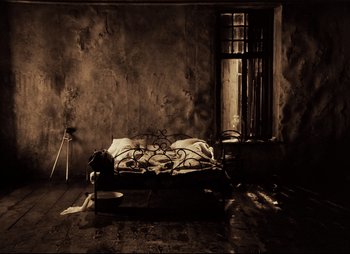 Movie still from “Stalker” (1979), directed by Andrei Tarkovsky – A bed in a room with a window and wooden floors; Wide shot, High angle