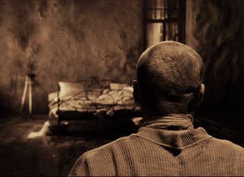 Movie still from “Stalker” (1979), directed by Andrei Tarkovsky – A man standing in front of a couch in a room; Medium shot, Over the shoulder angle