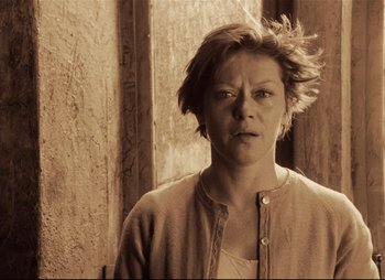 Movie still from “Stalker” (1979), directed by Andrei Tarkovsky – A woman with short brown hair is standing in front of a wall; Medium shot, Low angle