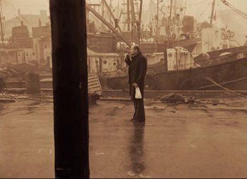 Movie still from “Stalker” (1979), directed by Andrei Tarkovsky – A man standing on a dock talking on a cell phone; Wide shot, High angle