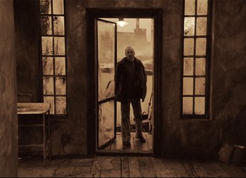 Movie still from “Stalker” (1979), directed by Andrei Tarkovsky – An older man standing in a doorway of an old building; Wide shot, Low angle