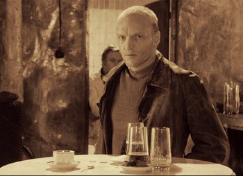Movie still from “Stalker” (1979), directed by Andrei Tarkovsky – A man sitting at a table in front of two glasses; Medium shot, Low angle