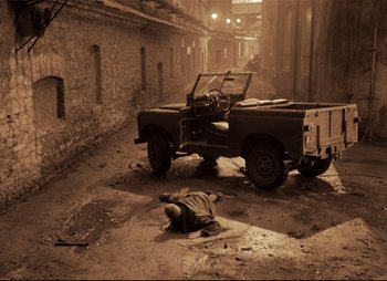 Movie still from “Stalker” (1979), directed by Andrei Tarkovsky – An old jeep is parked in the middle of the street; Wide shot, High angle