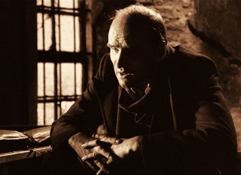 Movie still from “Stalker” (1979), directed by Andrei Tarkovsky – An older man sitting in a dark room with his hands crossed; Close Up shot, Low angle