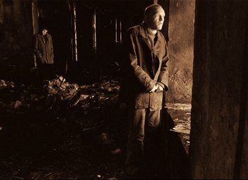 Movie still from “Stalker” (1979), directed by Andrei Tarkovsky – A man standing next to a pile of garbage; Wide shot, Low angle