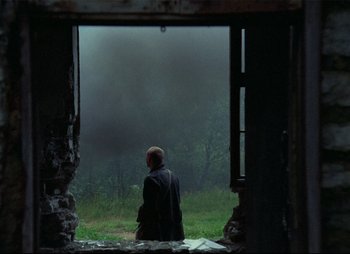 Movie still from “Stalker” (1979), directed by Andrei Tarkovsky – A man sitting in a doorway looking out a window; Wide shot, Over the shoulder angle