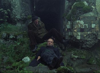 Movie still from “Stalker” (1979), directed by Andrei Tarkovsky – Two men are sitting on the ground in the dark; Wide shot, High angle