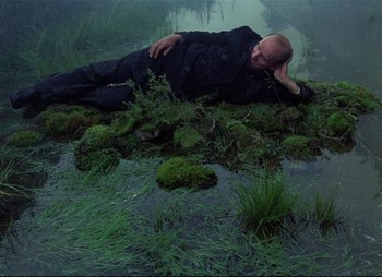 Movie still from “Stalker” (1979), directed by Andrei Tarkovsky – A man laying on the ground next to a body of water; Wide shot, High angle