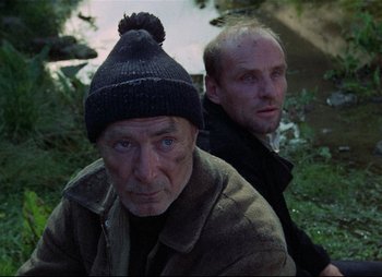 Movie still from “Stalker” (1979), directed by Andrei Tarkovsky – Two men are sitting next to a body of water; Close Up shot, Low angle