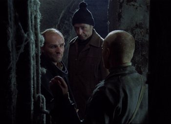 Movie still from “Stalker” (1979), directed by Andrei Tarkovsky – A group of men standing next to each other in a room; Medium shot, Over the shoulder angle