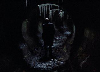 Movie still from “Stalker” (1979), directed by Andrei Tarkovsky – A man standing in a dark cave with icicles on the ground; Wide shot, High angle