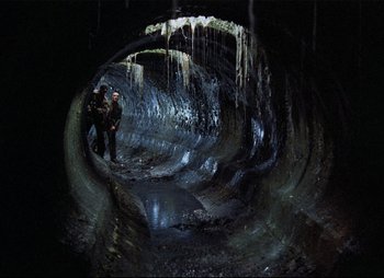 Movie still from “Stalker” (1979), directed by Andrei Tarkovsky – Two people are standing in a cave with icicles hanging from the ceiling; Wide shot, High angle