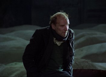 Movie still from “Stalker” (1979), directed by Andrei Tarkovsky – An older man sitting on a chair in a dark room; Medium shot, Low angle