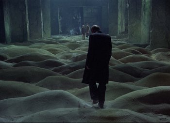 A man in a black suit walking through a field of sand