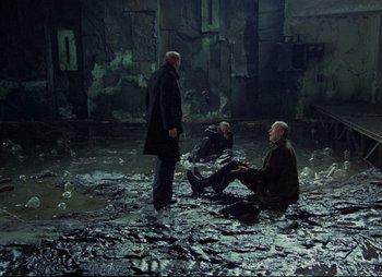 Movie still from “Stalker” (1979), directed by Andrei Tarkovsky – A group of men sitting on top of a wet ground; Wide shot, High angle