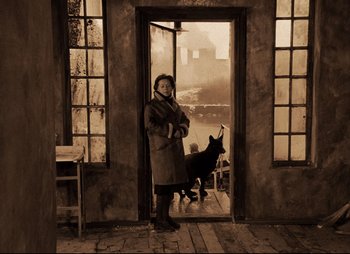 Movie still from “Stalker” (1979), directed by Andrei Tarkovsky – An old photo of a woman and a dog in front of an open door; Wide shot, Low angle