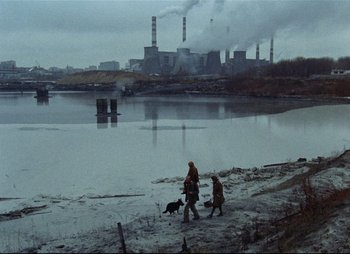 Movie still from “Stalker” (1979), directed by Andrei Tarkovsky – Two people walking a dog near a body of water; Extreme Wide shot, High angle