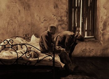 Movie still from “Stalker” (1979), directed by Andrei Tarkovsky – An old man sitting on a bed next to a cow; Wide shot, High angle