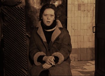Movie still from “Stalker” (1979), directed by Andrei Tarkovsky – A woman sitting on the ground with a cigarette in her mouth; Medium shot, High angle