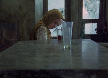 Movie still from “Stalker” (1979), directed by Andrei Tarkovsky – A woman sitting at a table in front of a glass of water; Medium shot, Over the shoulder angle