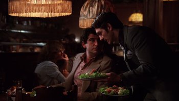 Movie still from “Star 80” (1983), directed by Bob Fosse – A man holding a tray of salad in front of another man and a woman; Medium shot, Over the shoulder angle
