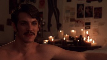 Movie still from “Star 80” (1983), directed by Bob Fosse – A shirtless man sitting in front of candles in a living room; Close Up shot, Over the shoulder angle