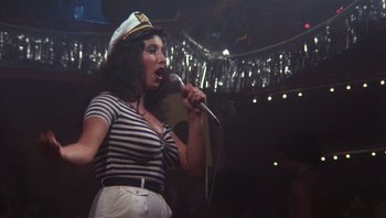 Movie still from “Star 80” (1983), directed by Bob Fosse – A woman wearing a sailor's hat is singing into a microphone; Medium shot, Low angle