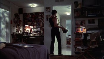 Movie still from “Star 80” (1983), directed by Bob Fosse – A man standing in a room holding a camera; Wide shot, High angle