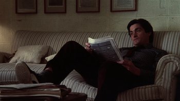 Movie still from “Star 80” (1983), directed by Bob Fosse – A man sitting on top of a couch while reading a newspaper; Medium shot, Low angle