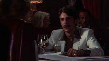 Movie still from “Star 80” (1983), directed by Bob Fosse – A man sitting at a table with a glass of wine in front of him; Close Up shot, Over the shoulder angle