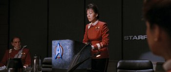 Movie still from “Star Trek VI: The Undiscovered Country” (1991), directed by Nicholas Meyer – A woman in a red jacket standing next to a box; Medium shot, Over the shoulder angle