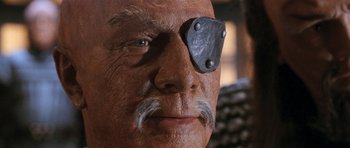 Movie still from “Star Trek VI: The Undiscovered Country” (1991), directed by Nicholas Meyer – An old man with a mustache and a beard has an eye patch on; Extreme Close Up shot, Over the shoulder angle