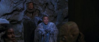 A man in a fur coat standing in front of a rock wall