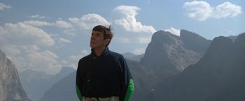 Movie still from “Star Trek V: The Final Frontier” (1989), directed by William Shatner – A man standing on top of a mountain with mountains in the background; Medium shot, Low angle