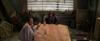 Movie still from “Star Trek V: The Final Frontier” (1989), directed by William Shatner – Two people sitting at a wooden table smoking and drinking; Medium shot, High angle