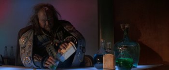 Movie still from “Star Trek V: The Final Frontier” (1989), directed by William Shatner – A man sitting at a table with a bottle of alcohol; Medium shot, Low angle