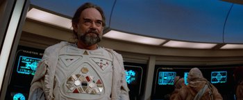 Movie still from “Star Trek V: The Final Frontier” (1989), directed by William Shatner – A man with a beard wearing a white outfit; Medium shot, Over the shoulder angle