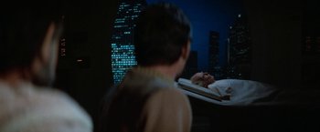 Movie still from “Star Trek V: The Final Frontier” (1989), directed by William Shatner – A man sitting on a bed in front of a city skyline at night; Medium shot, Over the shoulder angle