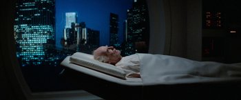 Movie still from “Star Trek V: The Final Frontier” (1989), directed by William Shatner – An older man laying in a bed in front of a city skyline at night; Medium shot, High angle