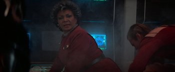 Movie still from “Star Trek V: The Final Frontier” (1989), directed by William Shatner – An older woman in a red jacket is standing in front of a computer screen; Medium shot, Over the shoulder angle