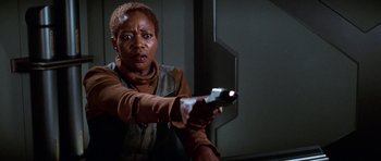 Movie still from “Star Trek: First Contact” (1996), directed by Jonathan Frakes – A woman is holding a gun in a room; Close Up shot, Over the shoulder angle