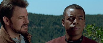 Movie still from “Star Trek: First Contact” (1996), directed by Jonathan Frakes – A person looking at the camera with trees in the background; Close Up shot, Low angle