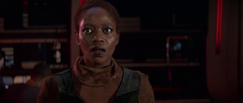 Movie still from “Star Trek: First Contact” (1996), directed by Jonathan Frakes – A young woman with short black hair wearing a brown jacket; Close Up shot, Over the shoulder angle