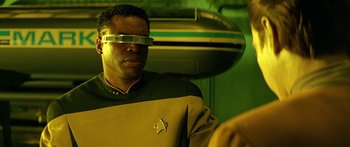 Movie still from “Star Trek: Generations” (1994), directed by David Carson – A man wearing a star trek uniform with a mirror on his forehead; Close Up shot, Over the shoulder angle