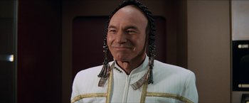 Movie still from “Star Trek: Insurrection” (1998), directed by Jonathan Frakes – A bald man wearing a white suit and a black and gold headpiece; Close Up shot, Over the shoulder angle